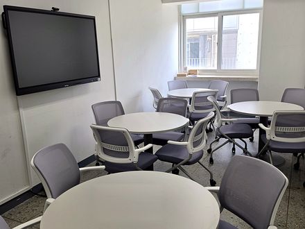 IDEA 라운지 내부. 원형 협업 테이블 4개와 이동식 의자, 전면 벽에 웹캠이 달린 대형 전자칠판이 설치되어 있습니다.